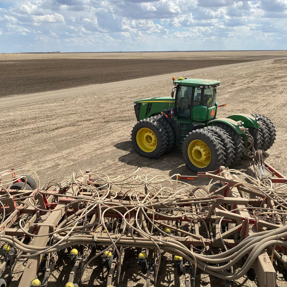 Green tractor on a plowed field with agricultural equipment.